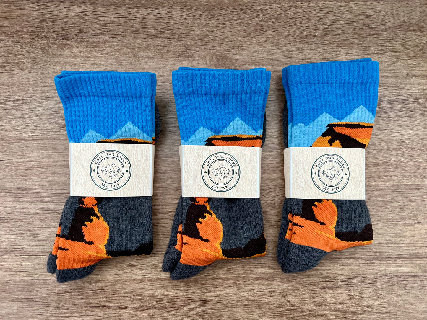 Three pairs of socks with Delicate Arch design on a wooden surface